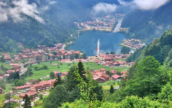uzungöl’ü yukarıdan gösteren panoramik manzara, göl çevresindeki cami, ahşap evler ve yeşil vadide yükselen sis bulutları